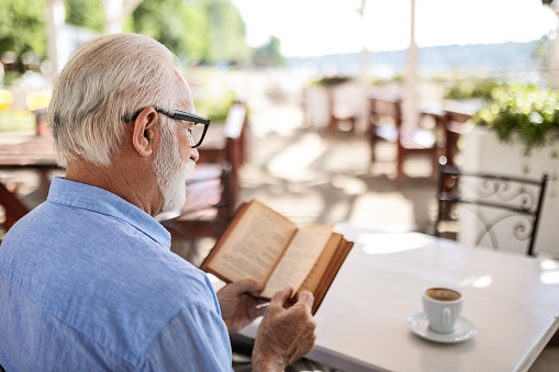 Senior man reading book while relaxing on chair at porch