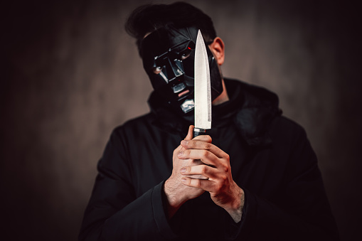 A hand of a murderer or robber holding a big knife and showing a sharp blade at night close up.