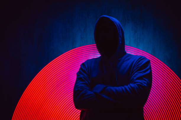 Scary Faceless Man In A Hoodie Under Neon Lights Scary faceless man in a hoodie standing under neon lights, with crossed arms. synthetic identity theft stock pictures, royalty-free photos & images