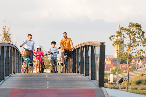 Young family with two children cycling at the city park in summer sunset
