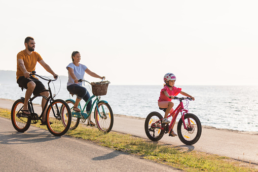 Mother, father and girl child having fun on vacation cycling near the sea. Family coastal bike ride.