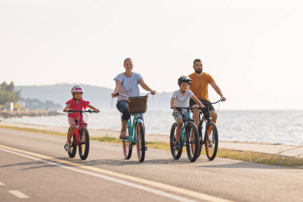 istock Two kids with parents riding bikes along a sea coastline, front view 1498928033