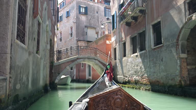 View from the front of the gondola of Venice canals, moored boats and architecture of the city during ride along one of the canals in Venice, Italy.