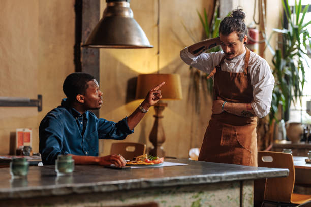 Angry African-American man complaining over dish to ashamed Hispanic waiter. Angry African-American man complaining about the service to a ashamed Hispanic waiter. black fussy pictures stock pictures, royalty-free photos & images