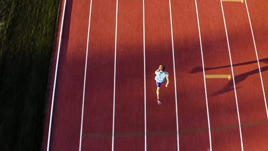 Caucasian male sprint runner alone on the athletic track, taking starting position and running in line four, aerial above shot.