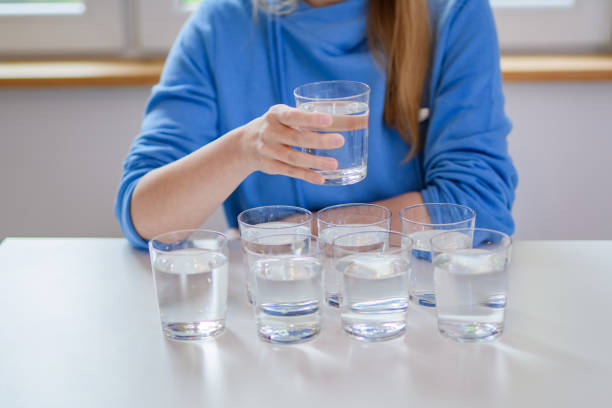 женщина пьет воду, перед ней стол с наполненными стаканами - water glass glasses number 8 стоковые фото и изображения