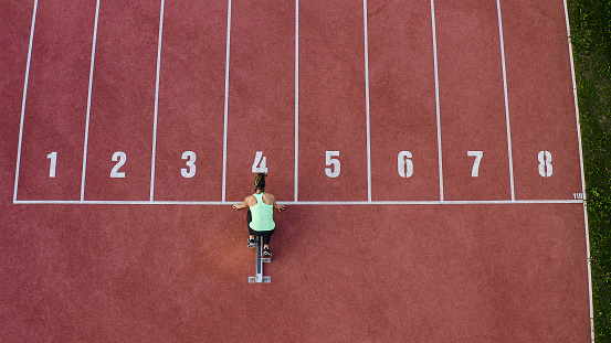 Caucasian female athlete alone on the athletic track, sprint running in line four, aerial directly above view.
