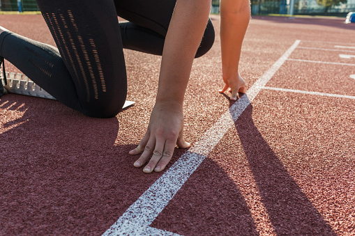 Caucasian woman at the athletic track starting point, hands on the start line and legs on starting block, ready set and go