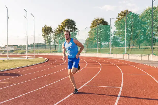 Photo of Young focused man running along an athletic track