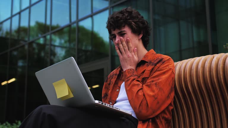 Man shocked by reading news on laptop screen while sitting outdoorsner moder business office. Shocked frightened man read bad news on internet, crisis and collapse in business concept.