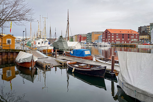 Trondheim, Norway - January 13, 2020: Marina with colorful houses in the background against cloudy sky