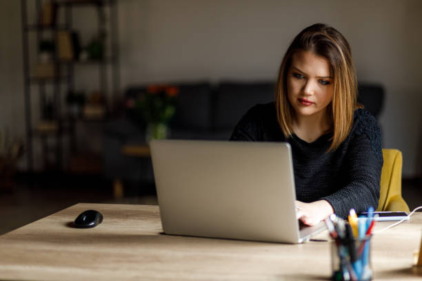 istock Diligent young woman sitting at her desk, typing data on laptop 1498943041
