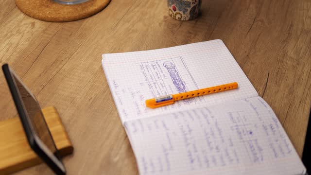 Open exercise book with notes, pen and smartphone lie on kitchen desk. Study work place with modern technology gadgets at home.