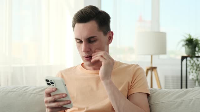 Puzzled man browsing phone on sofa in living room