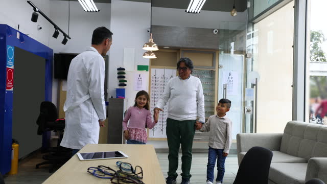 Latin American grandfather taking his grandkids to the optician for an eye exam
