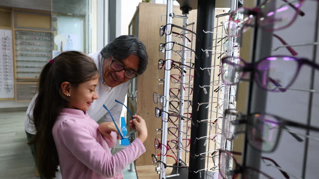 Happy Latin American girl shopping for eyeglasses with her grandfather at an optometry shop