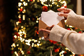 Young woman standing by the glistening Christmas tree and opening a letter