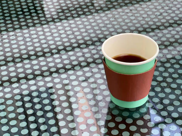 A disposable cup of beverage stands on a wet glass table