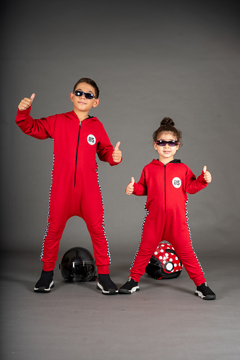 boy and girl are in racer costume on grey background helmets are background kids emotional vertical still