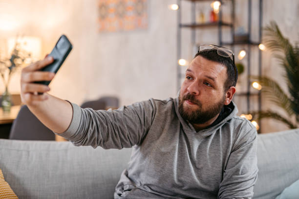 Young Man Taking A Selfie In His Living Room While Sitting