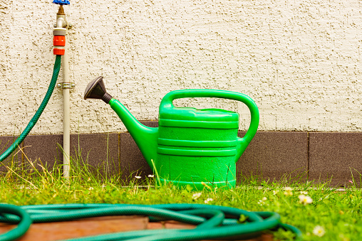 Gardening tools watering green can and tap with hose on garden plot.