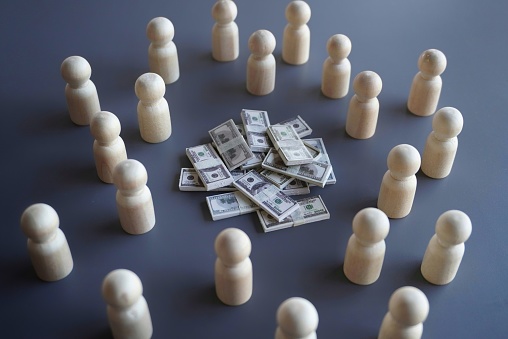 Group of wooden dolls and stack of money. Finance, donation, investor and crowdfunding concept