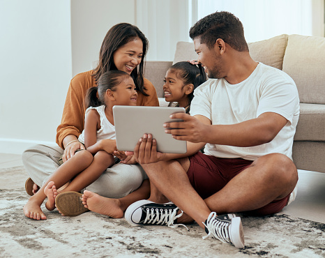 Family in living room, children smile with tablet video call online or streaming movies in Indonesia home. Indian mother sitting on floor, kids watch content on digital technology and happy father