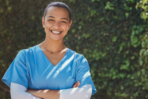 Portrait of a happy nurse standing in front of some greenery, during a beautiful sunny spring day