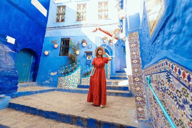Young woman with red dress visiting the blue city Chefchaouen, Marocco - Happy tourist walking in Moroccan city street - Travel and vacation lifestyle concept stock photo