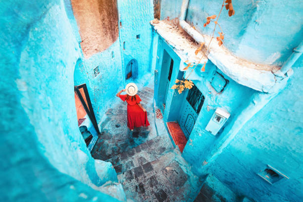 Young woman with red dress visiting the blue city Chefchaouen, Marocco - Happy tourist walking in Moroccan city street - Travel and vacation lifestyle concept stock photo
