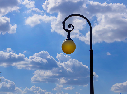 Round street lamp against the blue sky with white clouds.