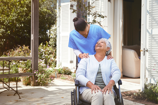 Nurse embracing her senior patient that sits in a wheelchair, outside during a beautiful spring day