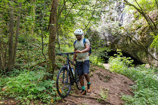 A black cyclist pushes a bicycle over inaccessible terrain in a mountain forest.