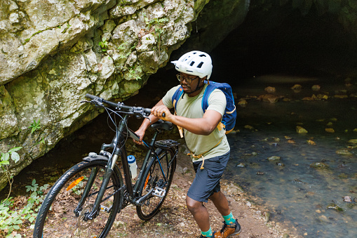 The cyclist comes out of the cave and pushes the bike.