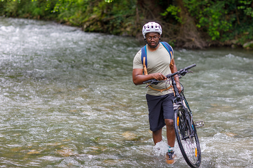 Young black biker crossing river with bike.