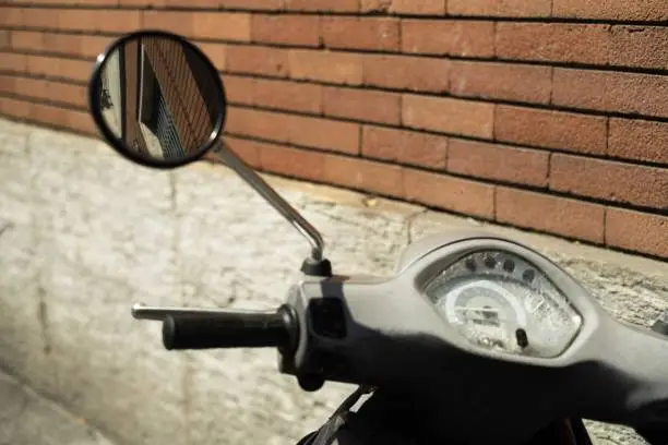A vintage motorcycle is parked in a modern urban environment with a textured brick wall in the background