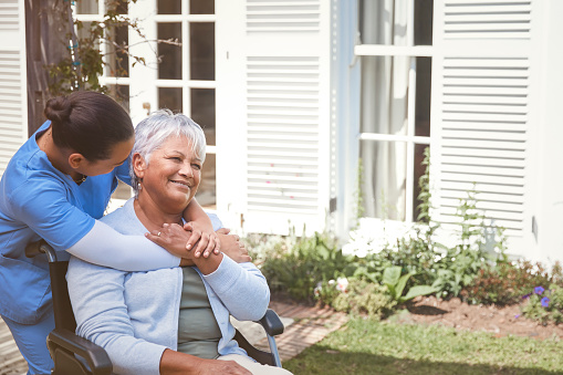 Nurse embracing her senior patient that sits in a wheelchair, outside during a beautiful spring day