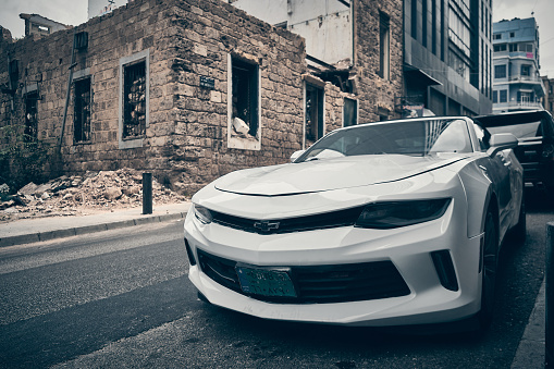 White Chevrolet Camaro parked on a city street opposite ruined residential building. Beirut, Lebanon - May 2023