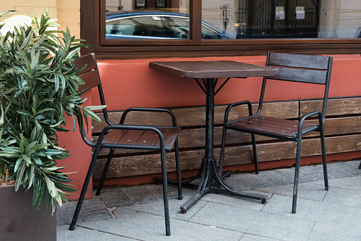 Wooden outdoor furniture - table and two chairs with metal legs at the entrance to the cafe. Outdoor veranda of a small private restaurant. Interior details.