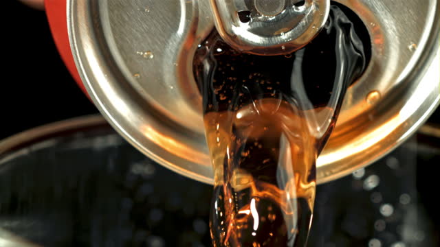 Cola is poured from a can into a glass.