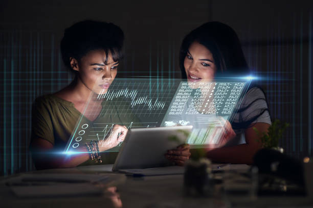 istock Teamwork, tablet hologram and business women in night office working on project. Forex, touchscreen and female employees working late on stock market, trading or finance investment in dark workplace. 1498983002