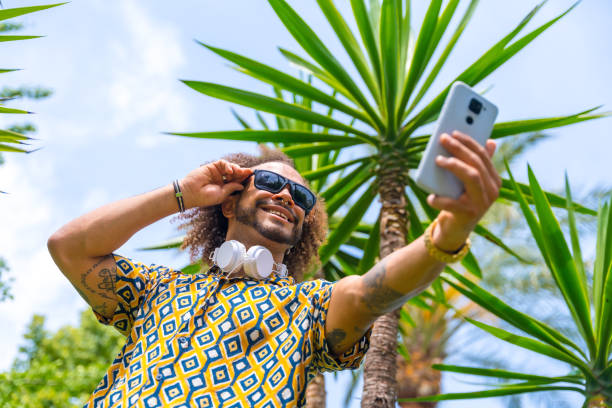 istock Afro-haired man on summer vacation next to some palm trees next to the beach taking a selfie. Travel and tourism concept 1498983767