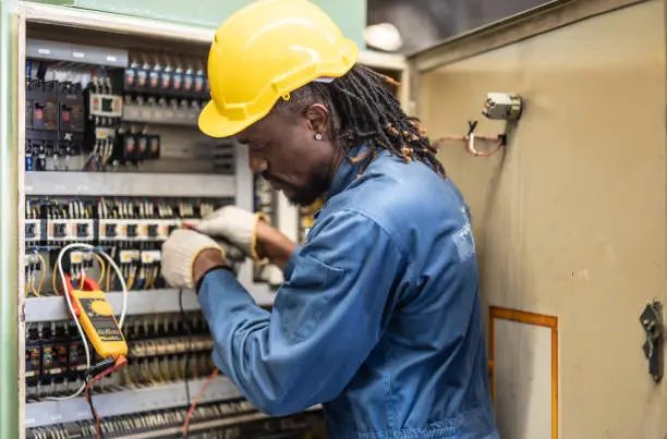Photo of Electrical technician tests wiring, polarity, grounding, voltages and performs electrical maintenance using hand tools that involve clamp meter, screwdriver, and cutter. The foreman's routine tasks.