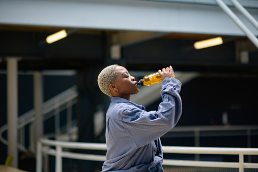 Beautiful young African woman drinking a soft drink indoors.  She has short blond dyed hair.