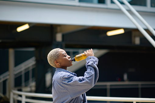 Beautiful young African woman drinking a soft drink indoors.  She has short blond dyed hair.