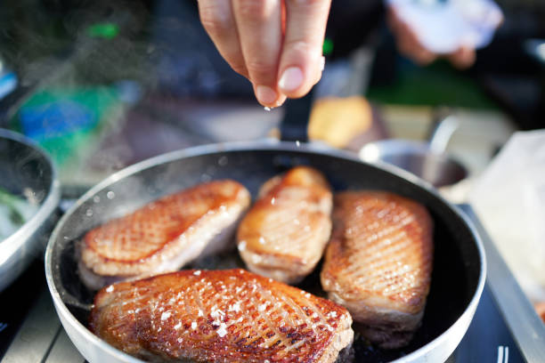 Duck breast being fried in hot pan with hand adding salt from the top