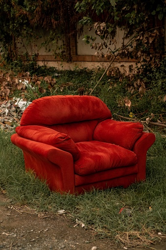 An abandoned red sofa, situated on a grassy area with a brick wall in the background, in a rural landscape