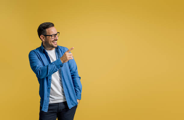 istock Happy businessman pointing away at copy space for advertisement while standing on yellow background 1498992720