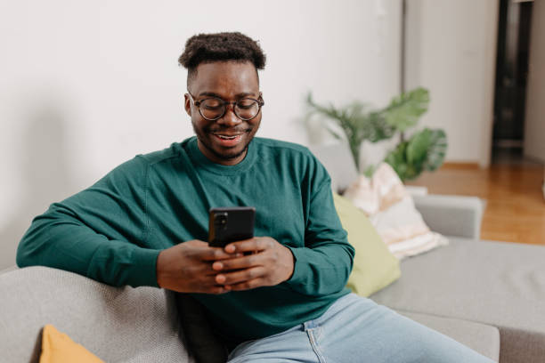 istock Contented Young Man Finds Serenity and Joy while Engrossed in his Mobile Phone on the Sofa 1498998500