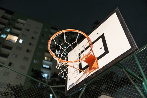 A close-up of a basketball hoop with an orange-colored rim and wire netting